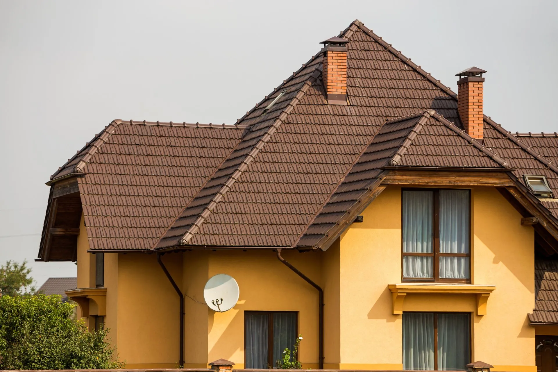 Yellow two-story home with brown tile roof and brick chimneys