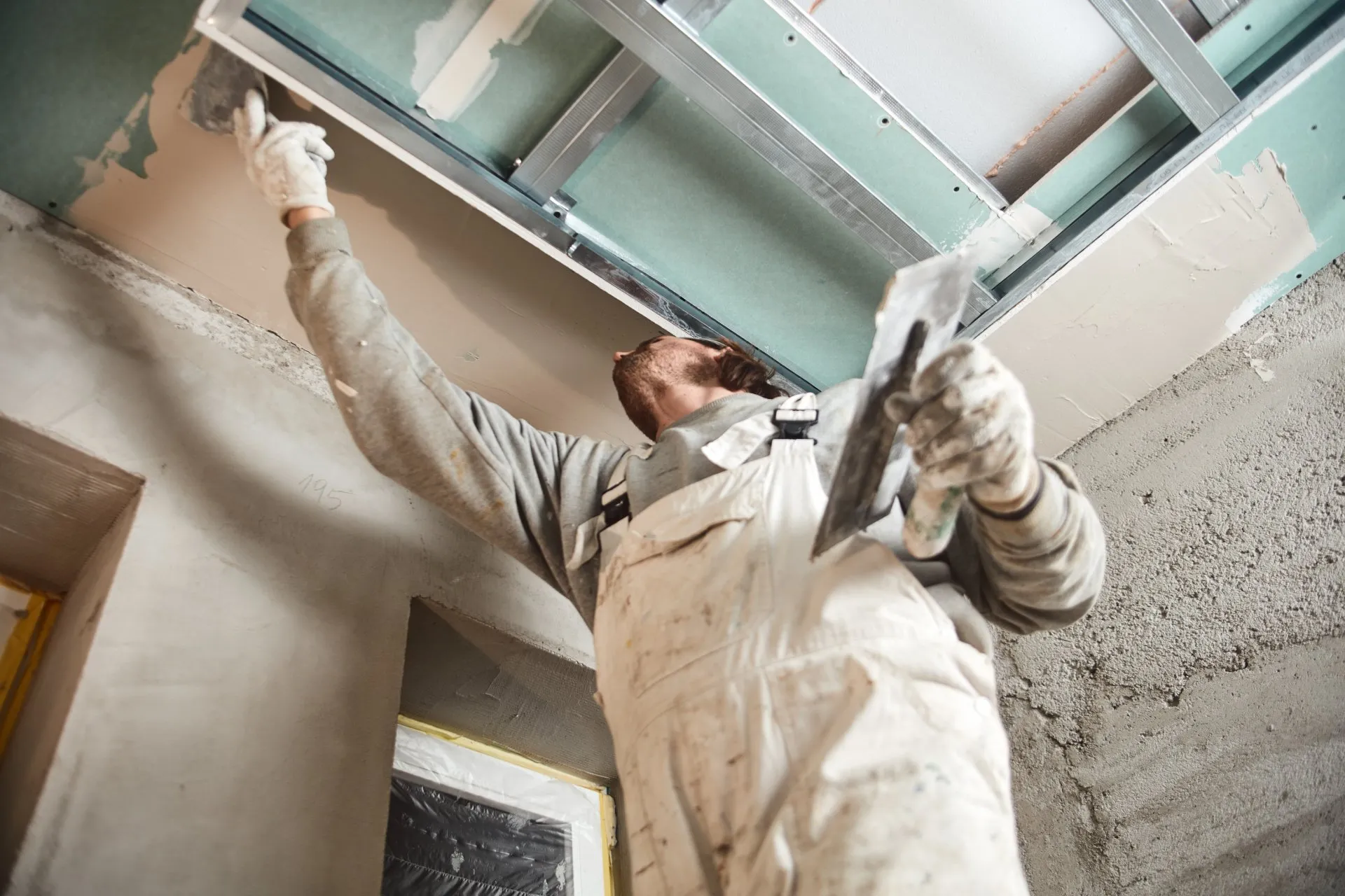 Worker in white overalls finishing a drywall ceiling with a trowel