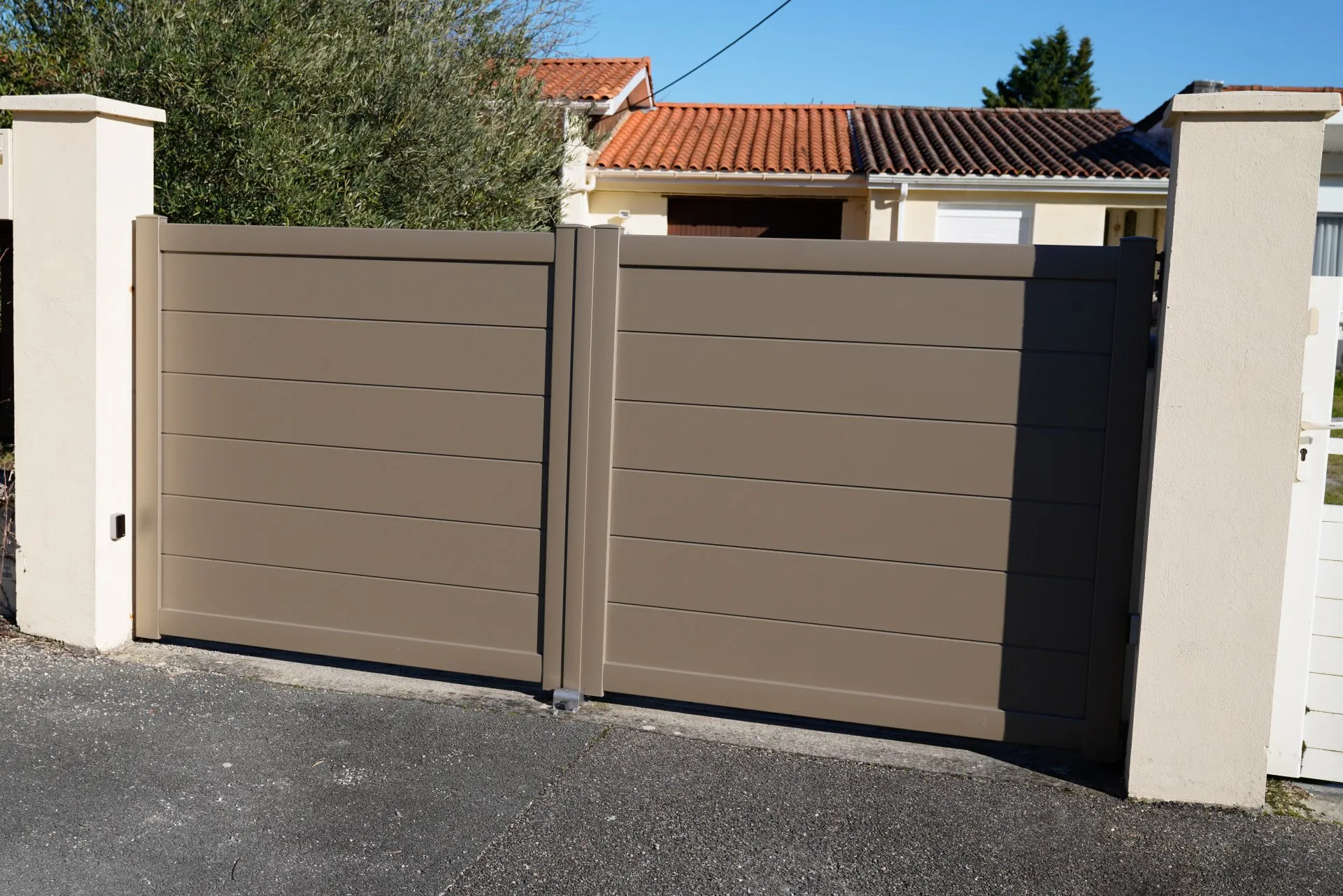 Taupe double driveway gate between cream stucco pillars