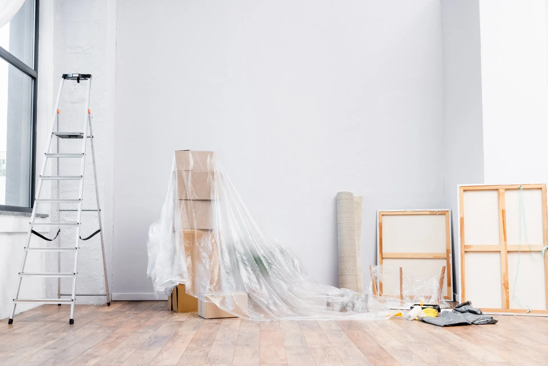 Empty white room prepped for painting with a ladder and plastic sheeting