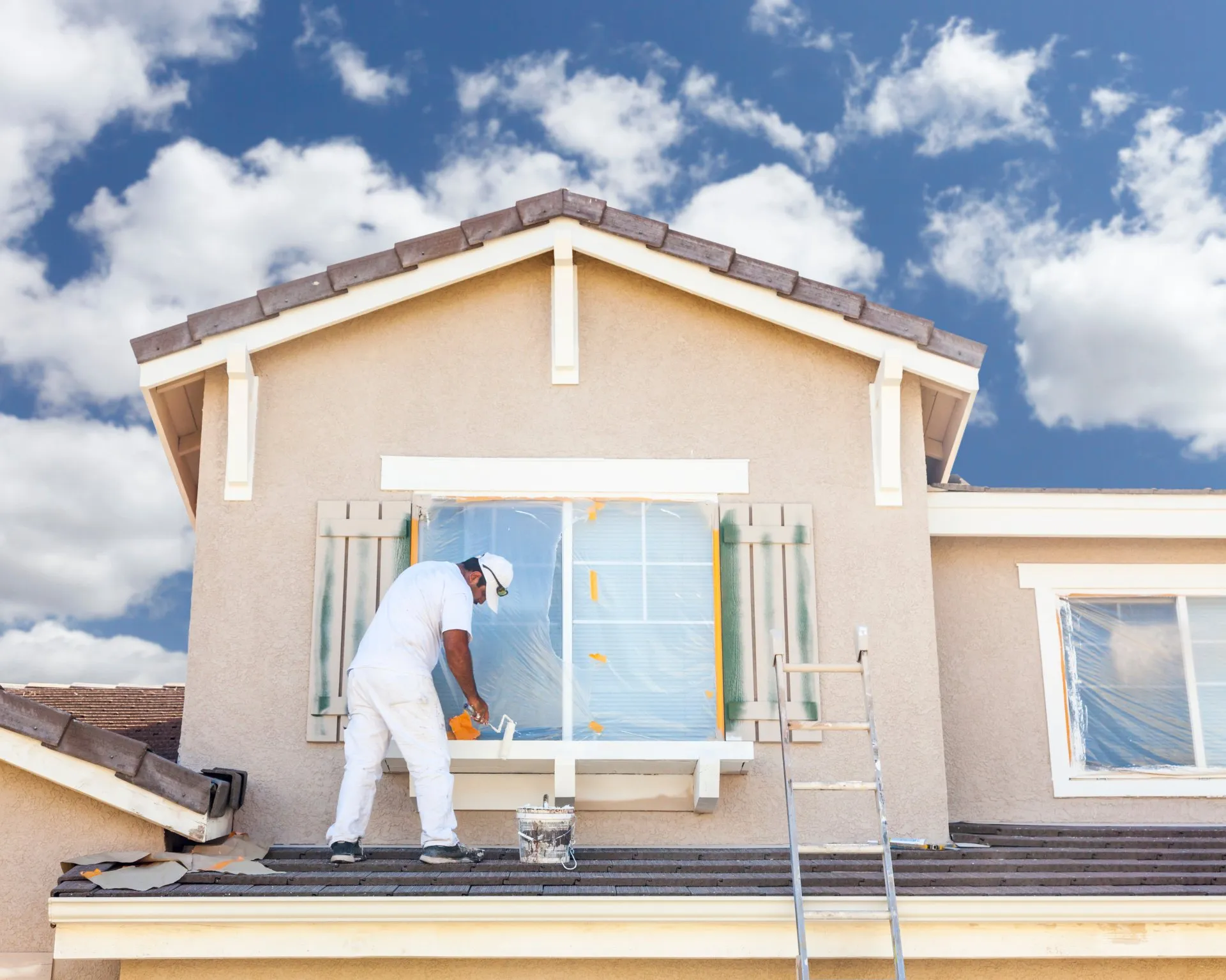 Painter in white coveralls masking a window on a stucco home