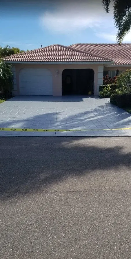 Peach stucco home with tile roof and a freshly coated gray driveway