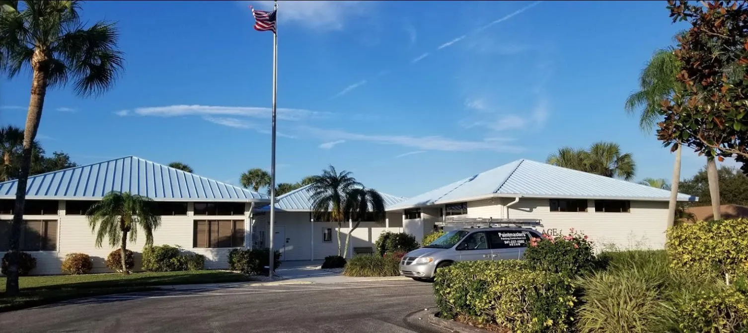 White single-story building with blue metal roofs, palm trees and flagpole