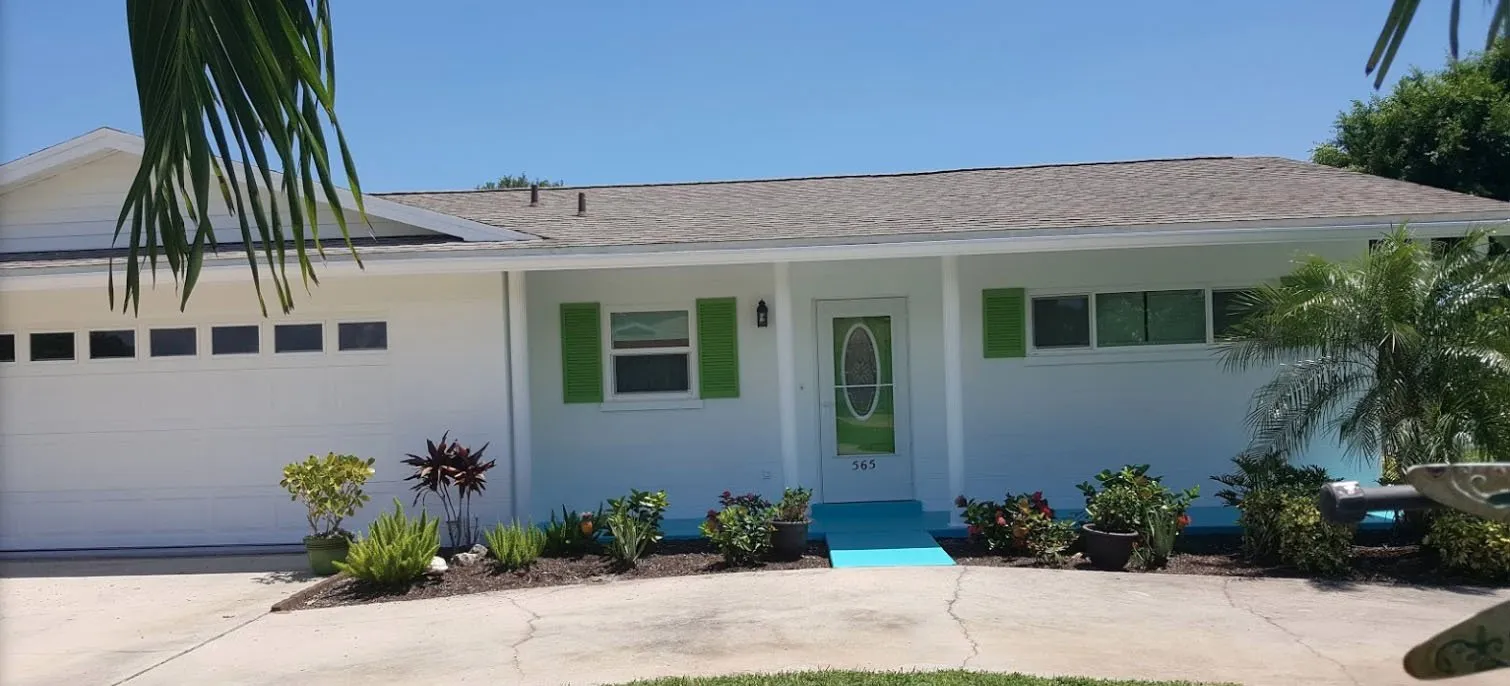 White single-story home with green shutters, green front door and tropical plants