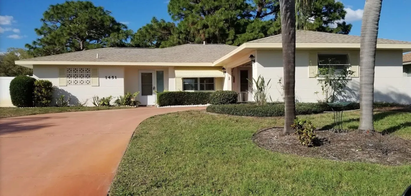 Cream ranch home with a red-coated curved driveway and palm trees