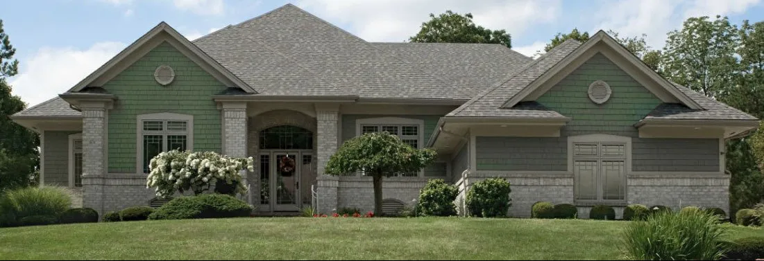 Sage green shingle-sided home with gray brick columns and white trim
