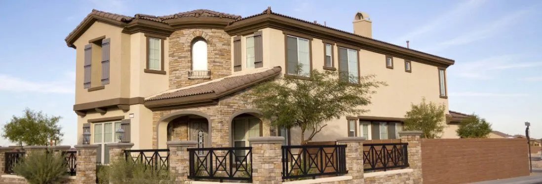 Two-story tan stucco home with brown shutters, stone accents and iron fence