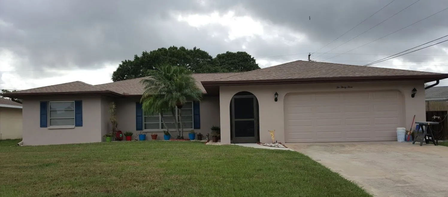 Tan stucco ranch home with blue shutters, palm tree and garage