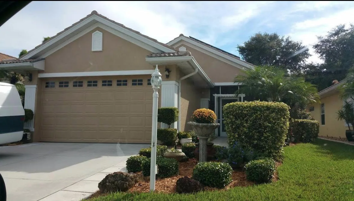Tan stucco home with white trim, garage and manicured shrubs