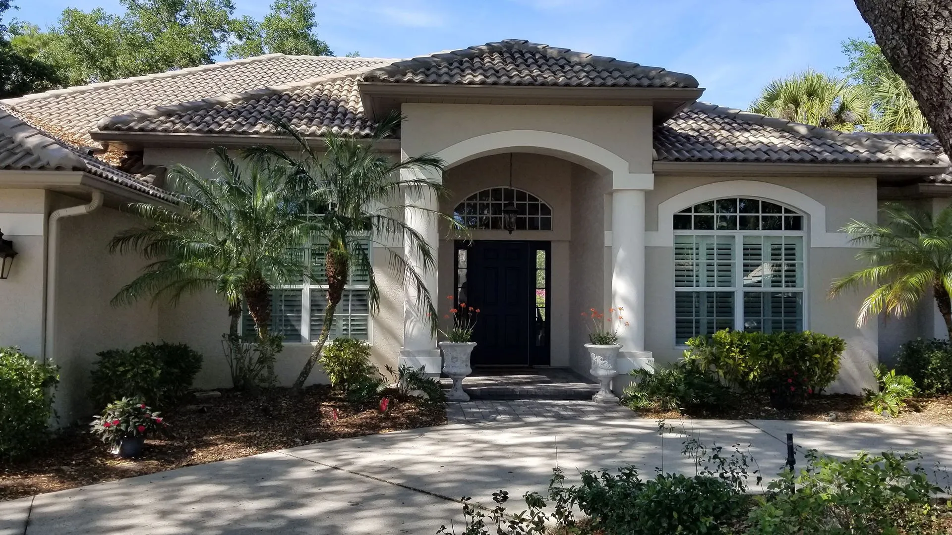 Beige stucco home with tile roof, arched entry and black front door