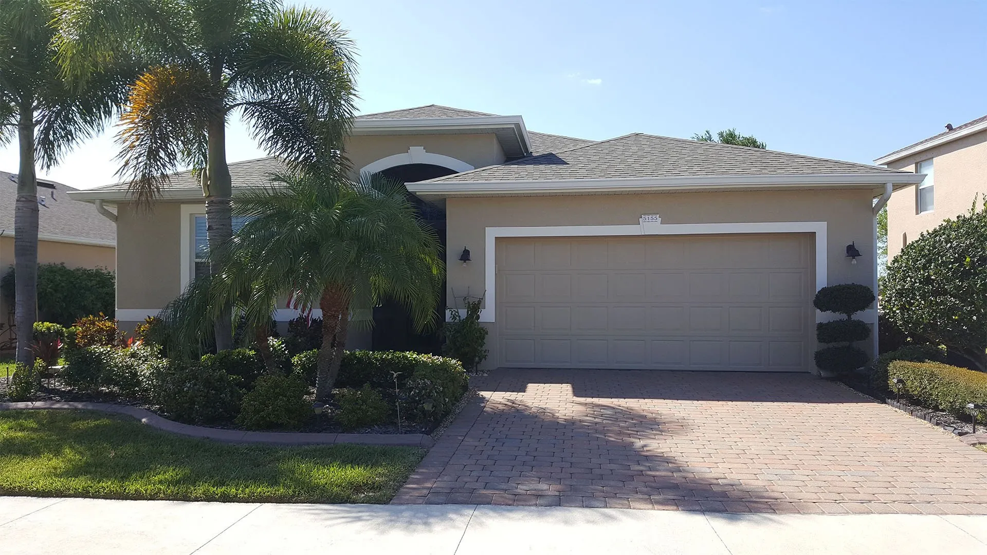 Tan stucco home with white trim, palm trees and paver driveway