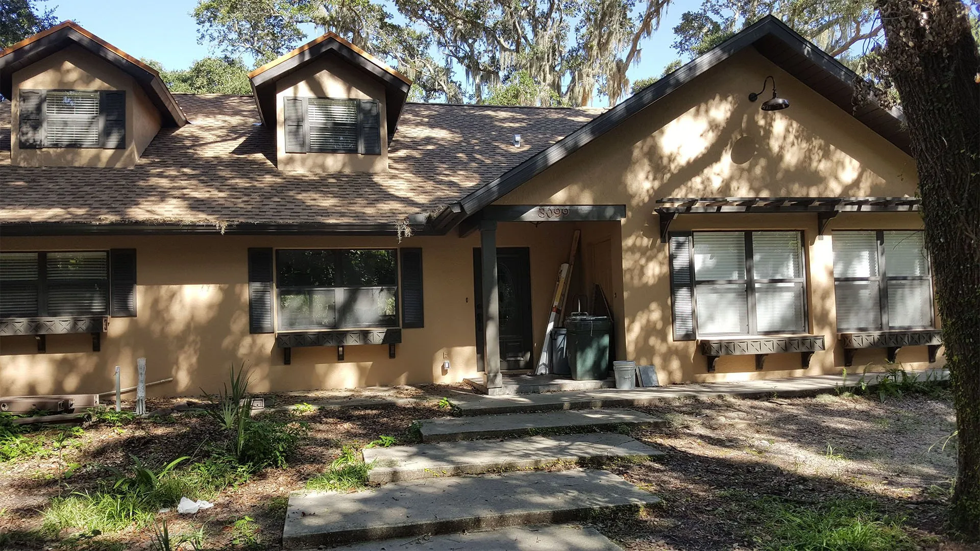 Tan stucco home with dark shutters, dormer windows and stone path steps